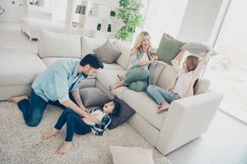 Photo of adopted family four members spend leisure time rejoicing pillows fight giggle sit couch...