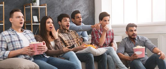 Multiethnic friends watching horror movie with popcorn at home