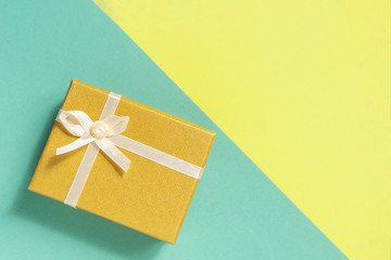 Yellow gift box with a bow on a two colored background. Top view.