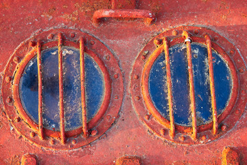 Two old rusty emergency exit hatch round windows (portholes) on the deck of abandoned ship or submarine on a red background