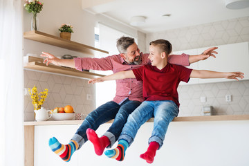 Mature father with small son sitting on kitchen counter indoors, having fun.