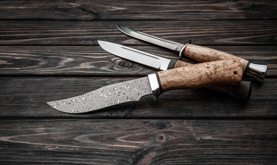 Hunting bowie knife with a wooden handle on dark wooden background. Steel arms weapon. top view