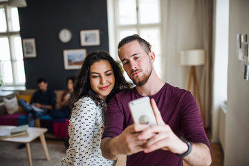 A group of young friends with smartphone indoors, taking selfie.