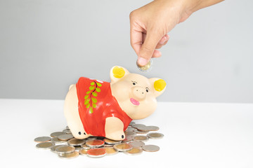 hand putting coin into Orange piggy bank saving money with coins pile