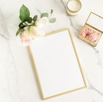 Golden frame mockup with a beautiful roses in a vase, candles on a marble table top view.  Copy space. Flat lay