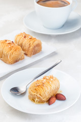 Greek pastry Kataifi with shredded filo dough stuffed with almond nuts, in honey syrup, on white plate, served with cup of coffee, vertical