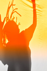 Shadow chelveka with dreadlocks and hands raised. Orange backlight