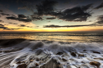 Obraz premium White waves crashing on the rocks at sunset