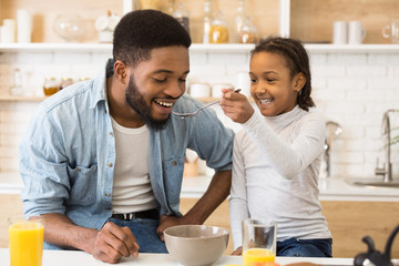 Adorable afro girl feeding her dad cereals
