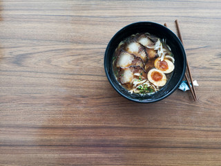A black bowl of Shoyu Ramen noodles with pork and eggs on wooden table
