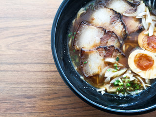 A black bowl of Shoyu Ramen noodles with pork and eggs on wooden table