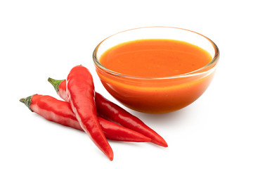 Peri peri chilli sauce in a glass bowl next to three red chillies isolated on white.