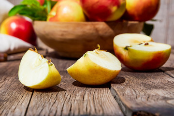 Naklejka na ściany i meble Fresh red apples with green leaves on a wooden old table. On a wooden background with sliced apple. Free space for text. soft focus