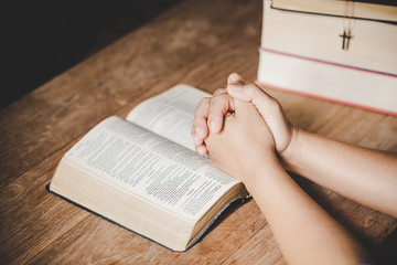 Spirituality and religion, Hands folded in prayer on a Holy Bible in church concept for faith. - obrazy, fototapety, plakaty