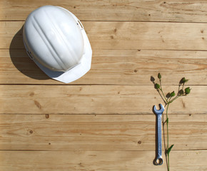 Male composition with white construction helmet and wrench on a wooden unpolished background