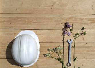 Construction helmet lies on a wooden background with flowers and tools.