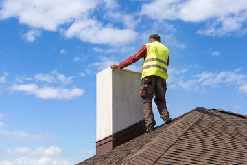 Man measuring chimney on roof top of new house under construction © brizmaker