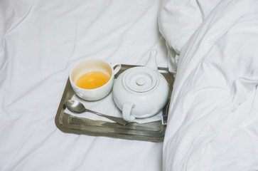 Fototapeta na wymiar Tea cup and kettle on the tray. Morning at the hotel. White linen sheets.