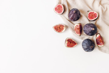 Decorative corner with fresh ripened purple figs and linen napkin. Creative composition of whole and sliced exotic fruit isolated on white table background. Flat lay, top view. Food photopfraphy.