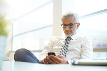 Relaxed businessman in shirt and tie working on cellphone in office