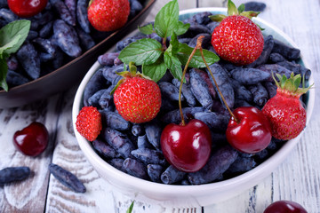 Honeysuckles, strawberries and cherries in white bowl on the table. Freshly picked berries