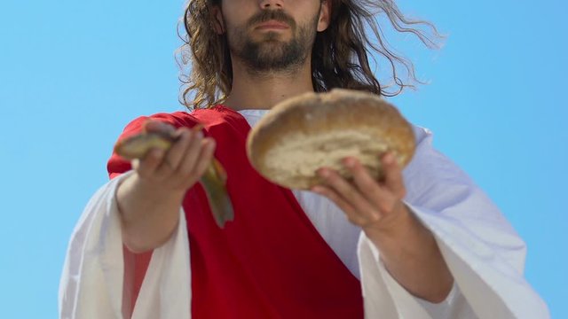 Saint Jesus Christ in robe stretching fish and bread into camera, son of God