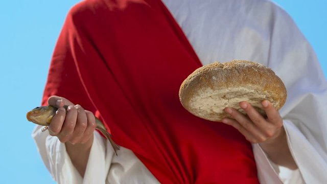 Monk in robe holding fish and bread, gifts from heaven, Jesus Christ sign