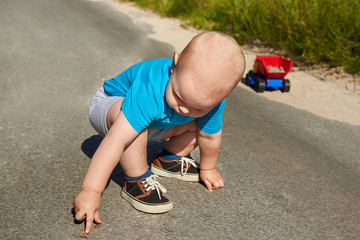 Little boy collects stones in a toy car on the pavement on a summer day