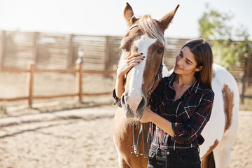 Lovely caucasian woman in checked shirt, hugging horse, horsewoman adore her pet, smiling gently, grooming animal as standing on farm near wooden fence in morning. Girl want become horsewoman - Powered by Adobe