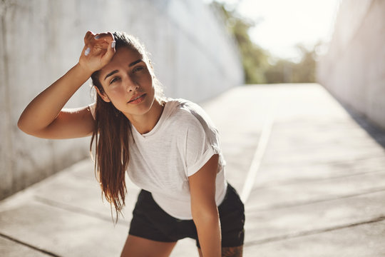 Sport, urban fitness and workout concept. Fit female athlete feel slight fatigue after morning run, wipe sweat from forehead taking breath before next lap, jogging to train body before marathon