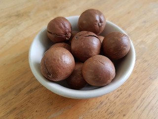 Unpeeled macadamia nuts in a white ceramic bowl on a wooden table 