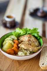 Boiled chicken leg and potatoes with zucchini, carrots and herbs served with bread and coffee on a wooden background