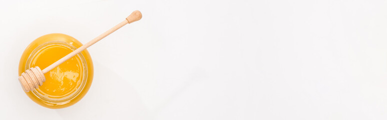 panoramic shot of jar with honey and wooden honey dipper on white background