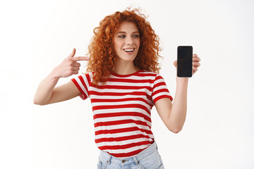 Good-looking happy bright redhead curly girl 25s hold smartphone pointing looking device display showing friend telephone screen awesome new application edit picture post online, white background