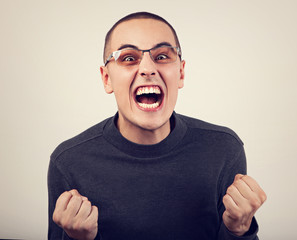 Angry young man shouting with open mouth and very anger face, showing the fists in fashion glasses