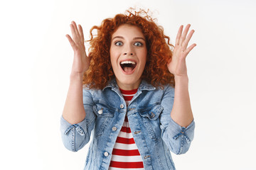 Excited amused attractive stylish redhead woman raising hands up fascinated wide eyes thrilled...