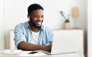 Smiling african-american guy in earphones studying foreign language online - obrazy, fototapety, plakaty