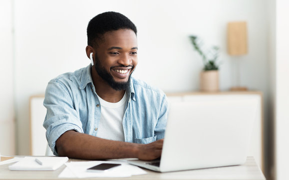 Smiling african-american guy in earphones studying foreign language online