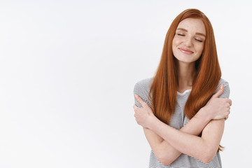 Fototapeta premium Dreamy lovely tender redhead european young woman, girlfriend dreaming sweet romantic embraces hugging herself close eyes smiling daydreaming have pleasant passionate thoughts desires