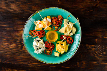 Wine appetizer set. parmesan cheese, dried tomatoes on round ceramic plate over wood backdrop, top view