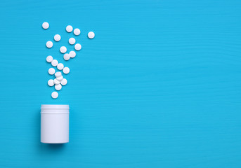 Pills and white bottle on blue background.