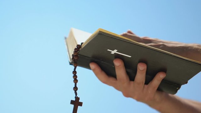 Male hands holding bible with rosary, priest praying celebrating mass, baptism