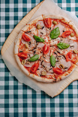 Neapolitan pizza with mushrooms, cheese, arugula, basil, tomatoes sprinkled with cheese on a wooden board on a tablecloth in a cell with a place for the text