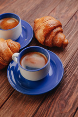 two cups of coffee and croissants on a wooden background, good light, morning atmosphere