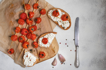 Grilled cherry tomatoes on skewers, on baking paper. Italian bruschetta with tomatoes and cheese