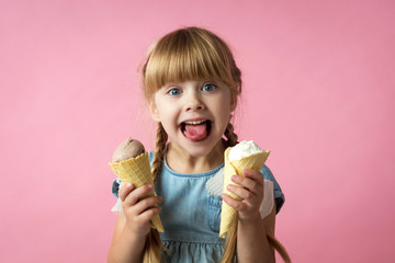 little girl with pigtails in a blue dress eating ice cream in a cone on a pink background