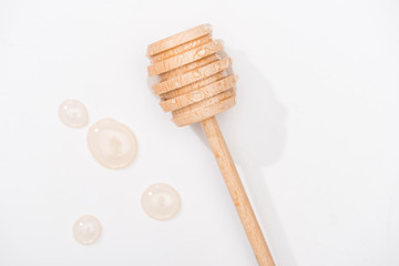 top view of honey drops and wooden honey dipper on white background