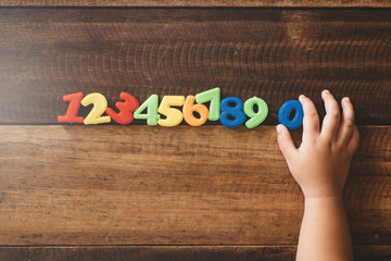 Child hand holding number zero with sets of other colorful numbers plastic toy on a wooden table. Concept of child learning numbers and child education