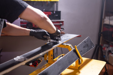 Repair, service and people concept - a man repairing the ski by rubbing a paraffin