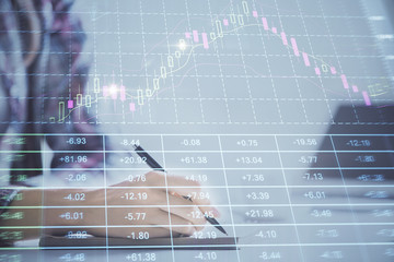 A woman hands writing information about stock market in notepad. Forex chart holograms in front....